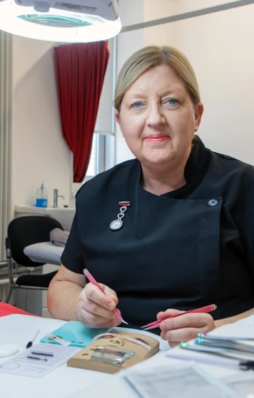 A beauty therapy student applies eyelash extensions to a mannequin head under a magnifying lamp in a professional training environment. A beauty therapy student applies eyelash extensions to a mannequin head under a magnifying lamp in a professional training environment.